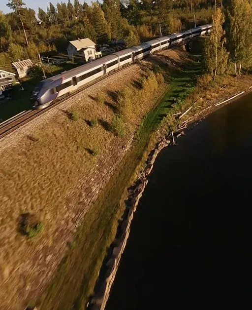 FPV-drone som jager et persontog langs et vann i kveldslys